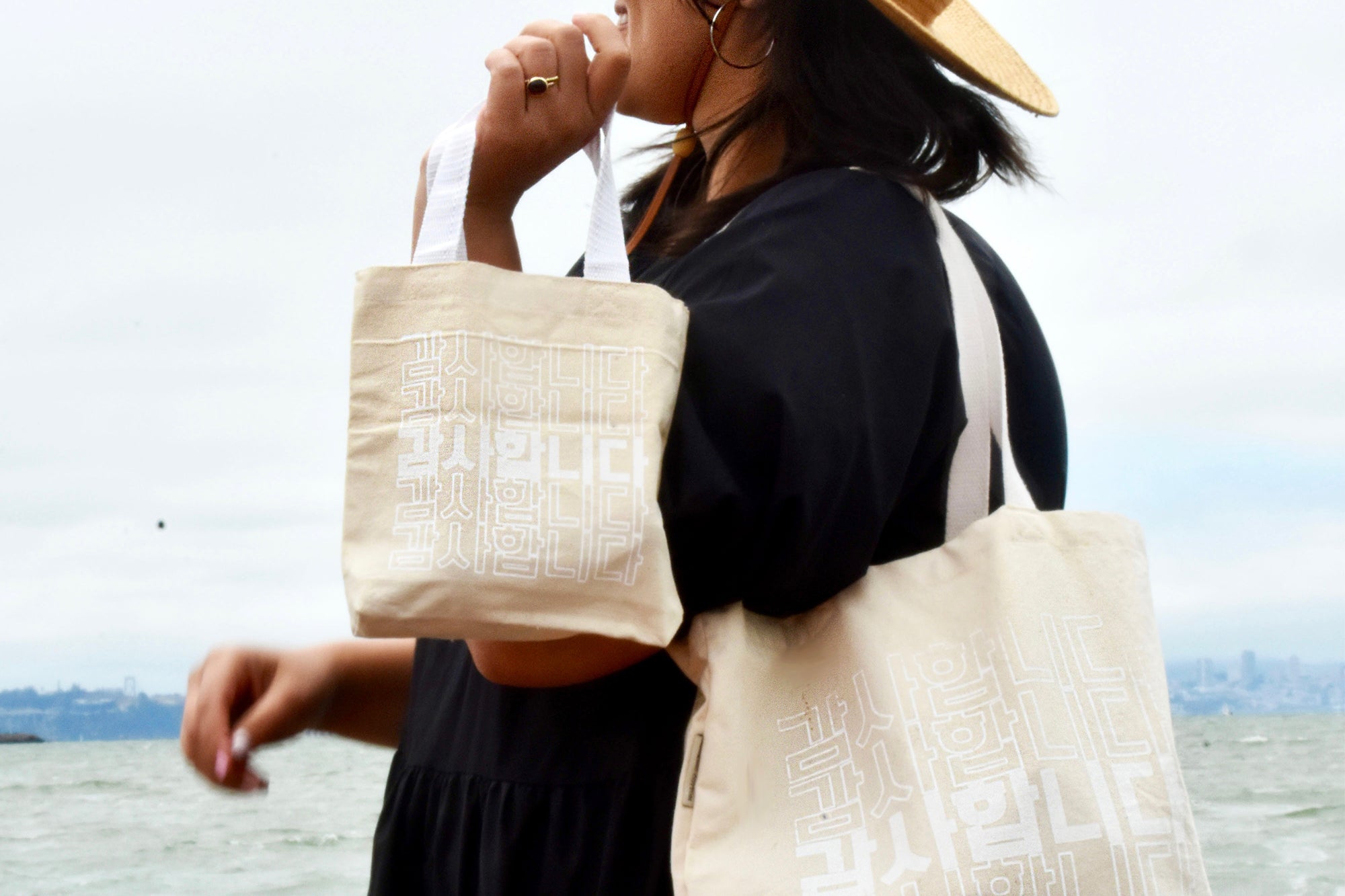 Stylish woman holding two canvas totes with white screenprint lettering in Korean reading "Thank You" 감사합니다